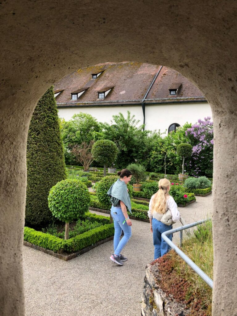 Two visitors walking through the garden viewed from a stone arch