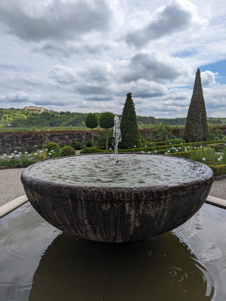 Stone fountain surrounded by neatly arranged garden beds and hedges